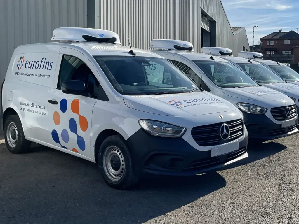 Row of Eurofins-branded refrigerated vans parked outside a warehouse, showcasing a fleet of temperature-controlled vehicles ready for nationwide food and water testing operations.
