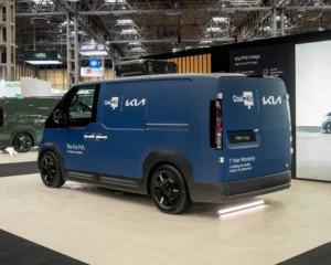 Kia PV5 fridge van displayed on CoolKit stand at commercial vehicle exhibition with surrounding booths and signage.